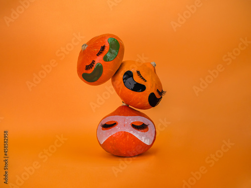Three pumpkin with eye patches, facial mask and towel on orange background, copy space. Skin care accessories, Halloween.