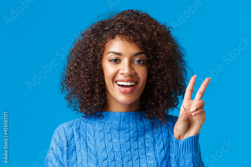 Close-up portrait carefree, happy joyful woman celebrating holidays, wishing everyone good new year, showing peace sign and smiling joyfully, express posivity and joy, wearing sweater photo