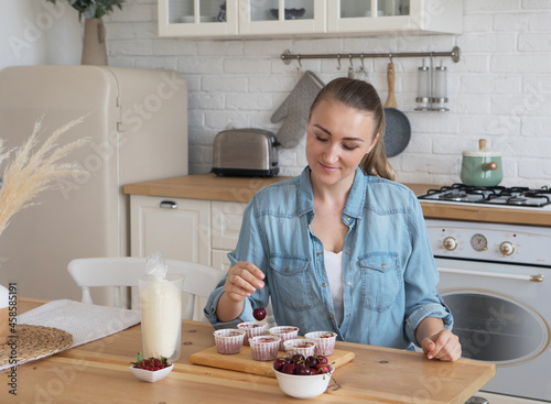Lifestyle, food, people and small business concept: A young woman decorates muffins with white cream and berries.