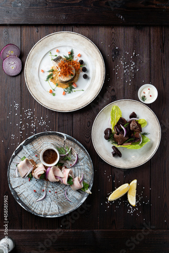 Assortment of meals in a mediterranean menu: pork shashlik, rollmops and pickled trout, straight above shot on a dark wooden table