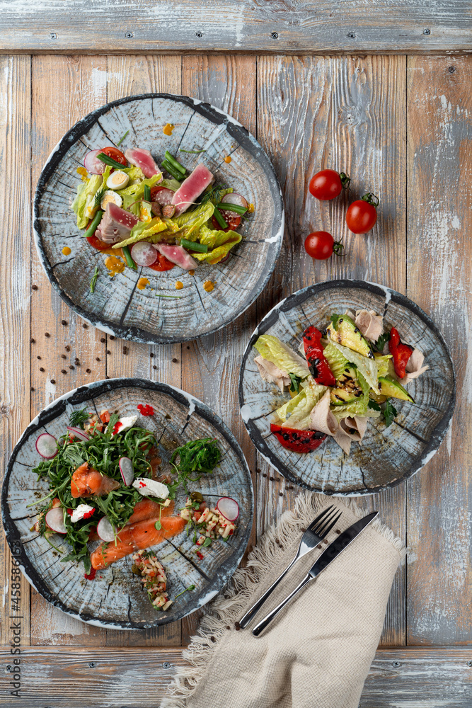 Mediterranean cuisine: smoked salmon salad, tuna salad and baked vegetables salad on wooden veranda Mediterranean cuisine: smoked salmon salad, tuna salad and baked vegetables salad on wooden veranda