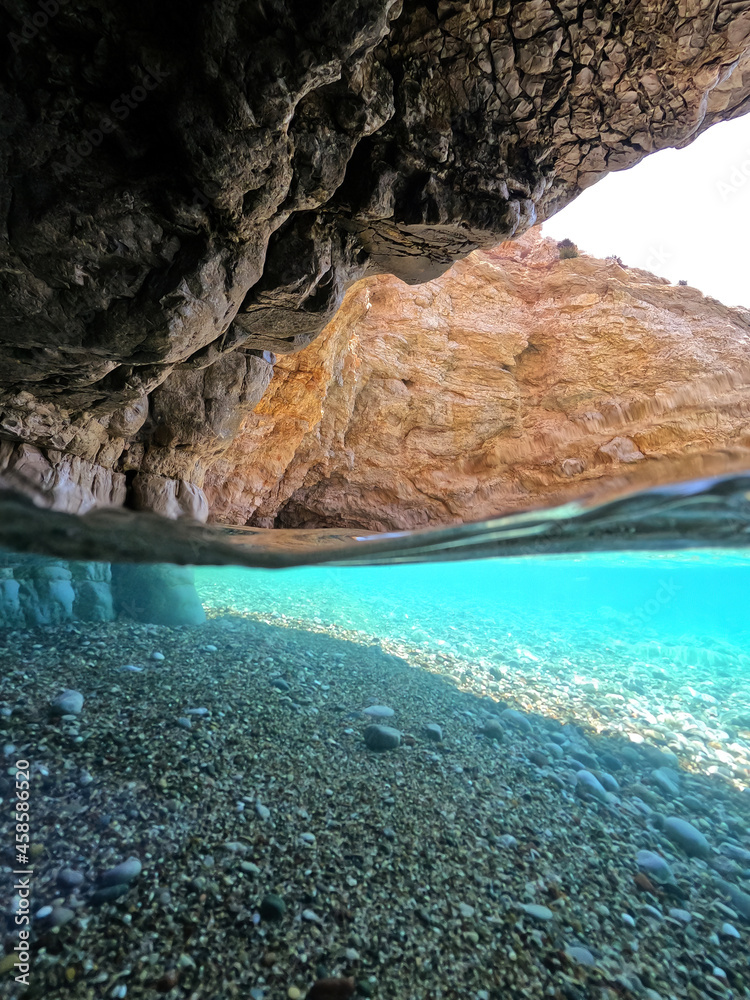 Underwater split photo of beautiful paradise pebble rocky bay of Kaladi with turquoise crystal clear sea and small caves, Kithira island, Ionian, Greece