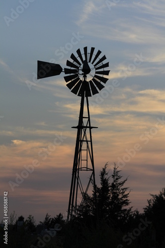 windmill at sunset with a colorful sky with white clouds out in the country west of Nickerson Kansas USA.
