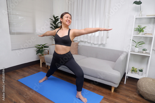 Young Asian women practicing yoga in the living room, Warrior II or Virabhadrasana II yoga pose.