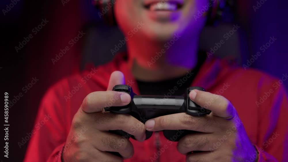 Close up male hands holding joystick game console. Young man playing video game online. Man in red jacket play computer pc at home in the dark room with neon light Close up male hands holding joystick game console. Young man playing video game online. Man in red jacket play computer pc at home in the dark room with neon light