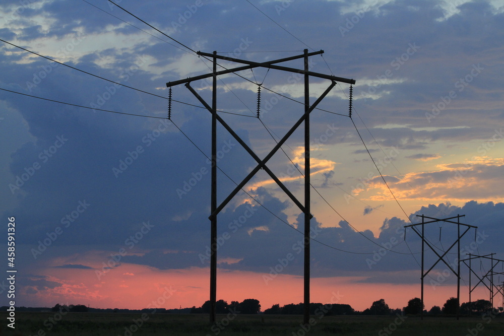 power lines at sunset with clouds and the Sun south of Sterling Kansas USA.