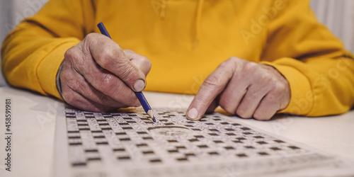 Obraz na płótnie Male wrinkled hand holding blue pencil and writing letter in crossword