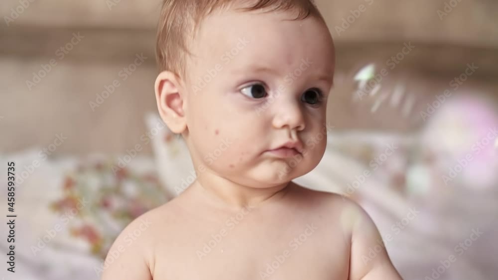 Caucasian blonde baby boy on a bed, playing with soap bubbles flying around. Slow motion Caucasian blonde baby boy on a bed, playing with soap bubbles flying around. Slow motion