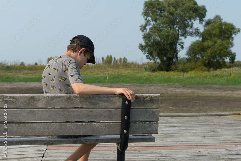 Boy with Autism and low muscle tone sits on a park bench; he takes a break while on a family walk at a nature preserve
