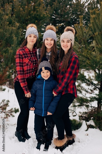 Three sisters in checkered shirts and a younger brother. Snowy winter forest. Family walks in the woods. Christmas family days
