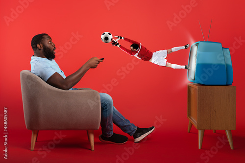 Soccer goalkeeper jumping out of television while a viewer is watching a game