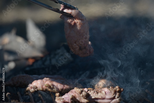Metal clamp grabbing chinchulines and molleja, cooked on the coals in a grill. photo