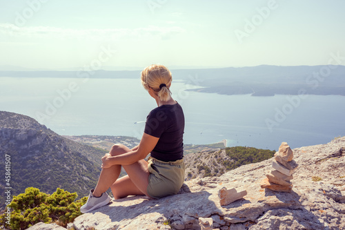 Fototapeta Naklejka Na Ścianę i Meble -  A girl sits on the edge of a cliff and looks at the sea. The girl looks from the mountain to the beach zlatni 