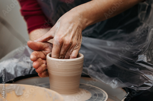 Close up of woman hands molding clay mug spinning on pottery wheel.