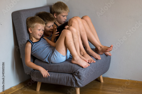 Three baby boys sit on chair and play with computer tablet