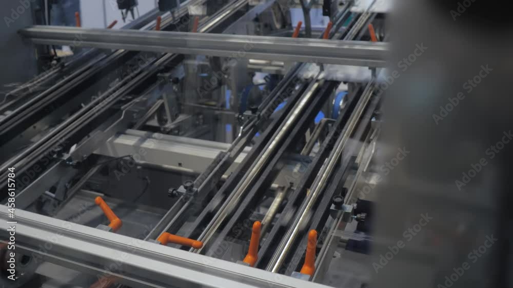 White cardboard sheet moving fast on conveyor line of automatic carton box making machine at food package exhibition, trade show. Industrial, equipment, technology concept
