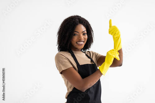 Young african woman hausewife cleaning with yellow gloves giving a thumbs-up isolated on white background. Happy cleaner having fun.