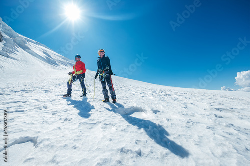 Two smiling young women Rope team descending Mont blanc du Tacul summit 4248m dressed mountaineering clothes with ice axes standing on snowy slope. People extreme activities sporty concept image.