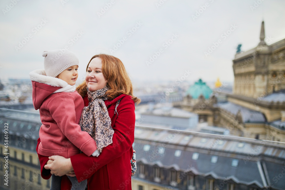 Young woman holding adorable todler girl while enjoying the view from Parisian rooftop terrace
