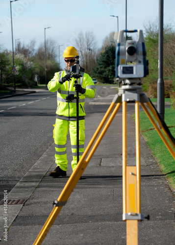фотографія Land surveyor performing initial survey of the road levels and kerb lines before start of construction works using robotic tacheometer controlled by remote control and prism on pogo