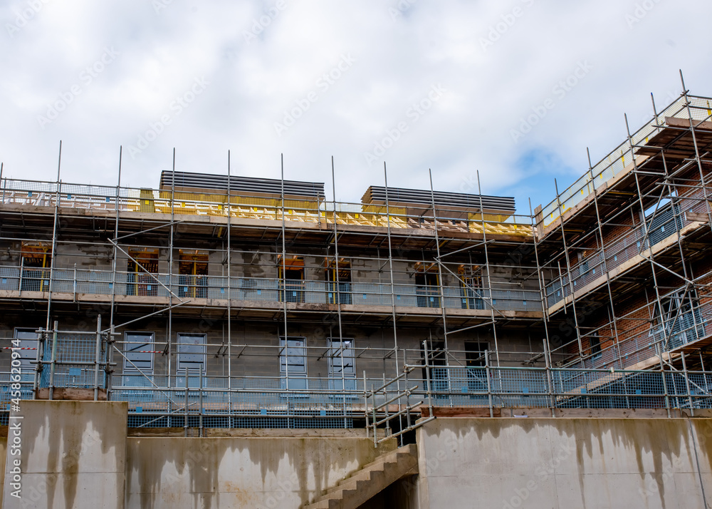 Scaffolds erected around new multistorey brick house on new residential housing development site to allow safe acces to place of work and windows and roof installation