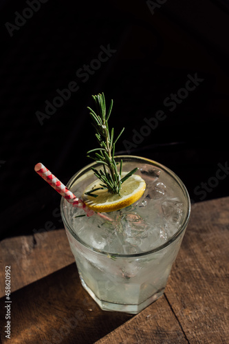 rosemary lemonade soda cocktail with ice and picnic gingham drinking straw on whiskey barrel happy hour