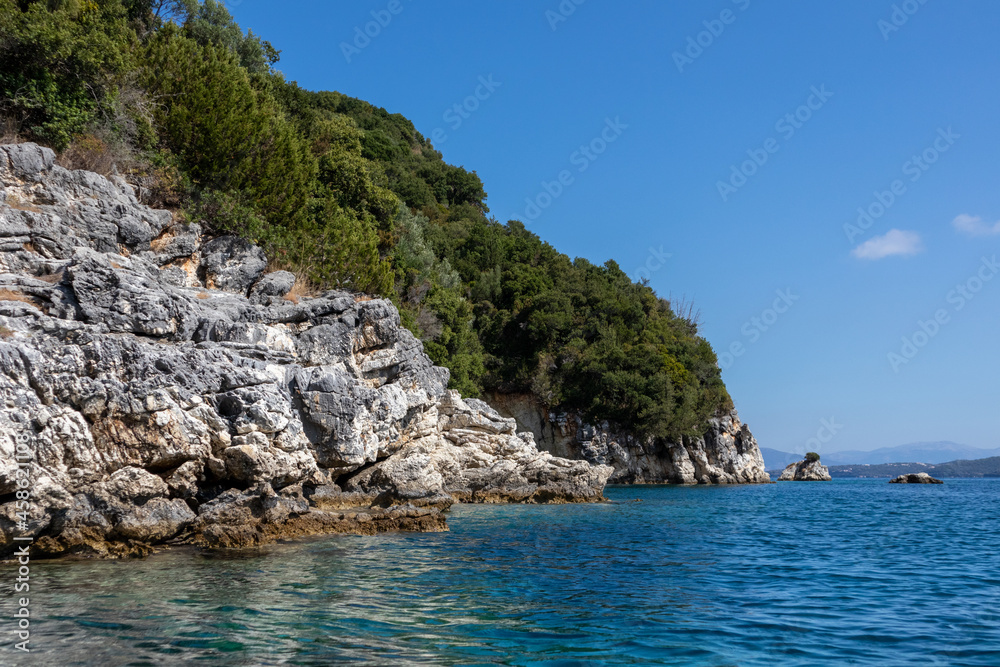 Blue sunny Ionian Sea with scenic green rocky cliffs coast and bright sky. Nature of Lefkada island in Greece. Summer vacation idyllic Ormos Desimi travel destination