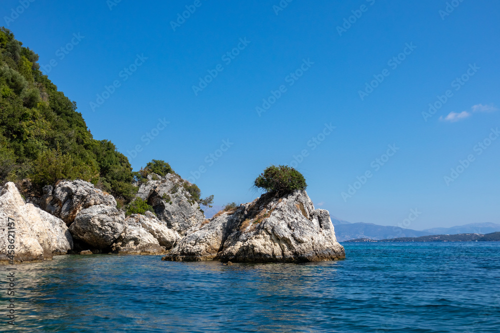 Scenic rocks in blue water of Ionian Sea with green cliffs and bright sky. Nature of Ormos Desimi, Lefkada island in Greece. Summer vacation travel destination