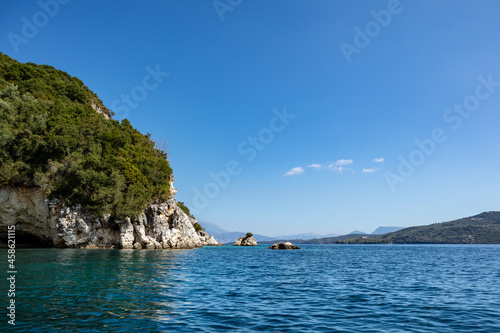 Blue clear calm Ionian Sea in Ormos Desimi with scenic green rocky cliffs coast and bright sky. Nature of Lefkada island in Greece. Summer vacation idyllic travel destination