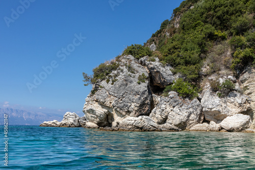 Scenic rocks in blue water of Ionian Sea with green cliffs and bright sky. Nature of island in Greece. Summer vacation travel destination