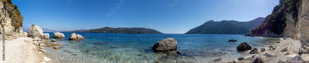 Wide panorama of white pebbles and rocks beach with azure clear water on coast of Lefkada island in Greece. Summer nature travel to Ionian Sea