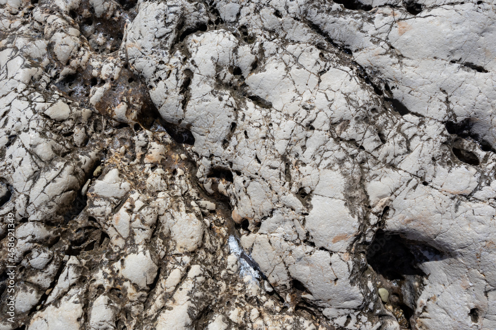 Fototapeta premium White and black natural marble rock material with cracks close-up texture. Light stone surface pattern details in sunny Greece