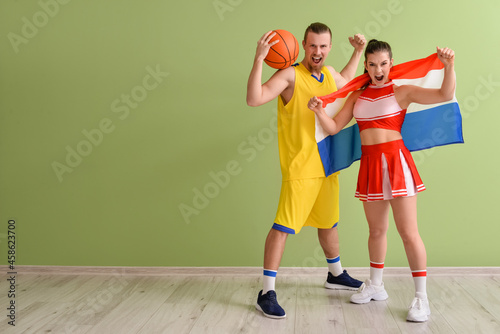 Cheerleader and basketball player with flag near color wall