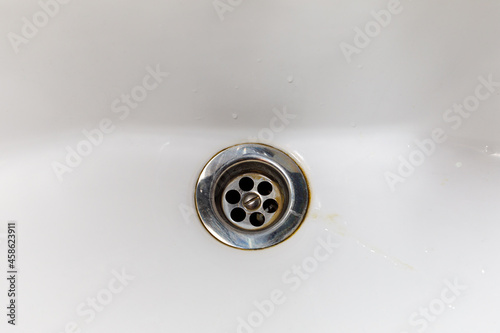 the drain hole of a white enameled bathroom with traces of dirt and rust