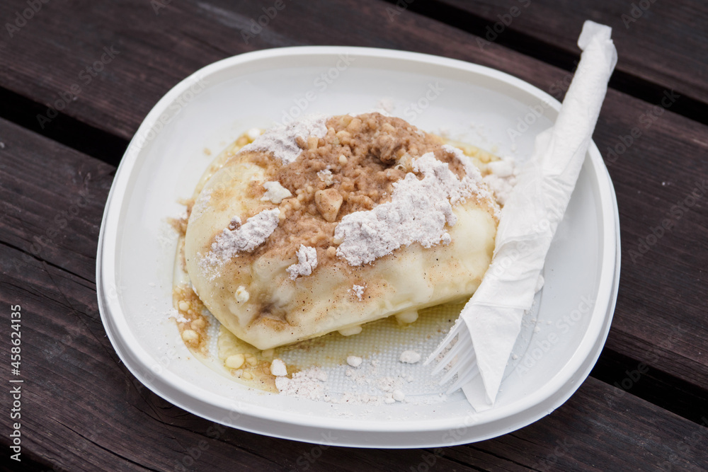 One large sweet stuffed dumpling with sugar and cinnamon with cutlery and a plate. One large sweet stuffed dumpling with sugar and cinnamon with cutlery and a plate.