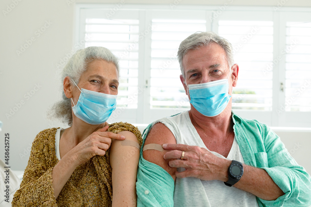 Fototapeta premium Smiling caucasian senior couple with plaster on arm after vaccination, wearing face masks
