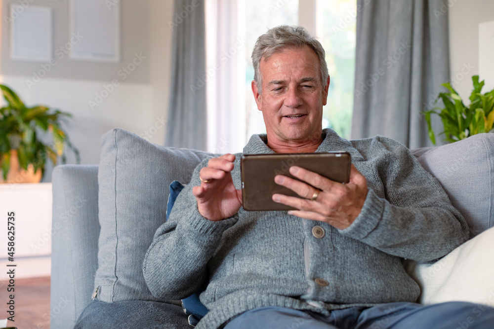 Happy caucasian senior man sitting on sofa and using tablet