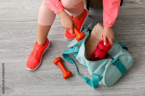 Woman in sport shoes preparing bag for training on light wooden background