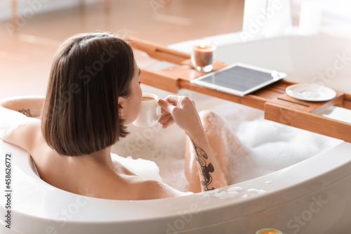 Young woman drinking coffee while taking bath at home