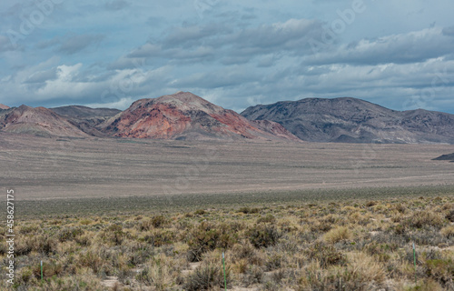 High Desert, Nevada, USA - May 17, 2011: Wide landscape of high mineral rich colored mountain under blue cloudscape, and green brown dunes in front.