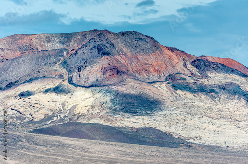 High Desert, Nevada, USA - May 17, 2011: Closeup of high mineral rich colored mountain and black hill under blue cloudscape.