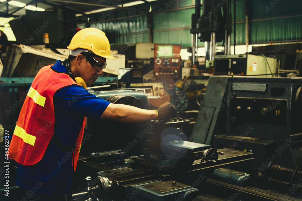 Male worker of engineering, lathing technician, wearing safety glasses, operating lathe, working overtime in an industrial factory Selective focus Male worker of engineering, lathing technician, wearing safety glasses, operating lathe, working overtime in an industrial factory Selective focus