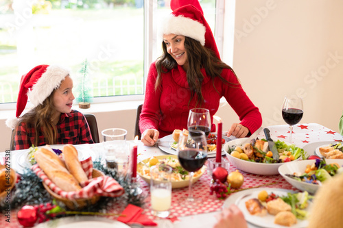 Happymother and daughter wearing santa hats sitting at christmas table