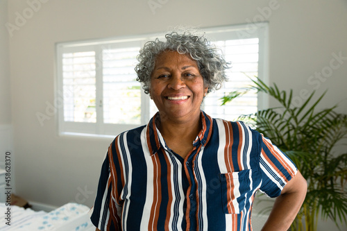 Happy african american senior woman standing in bedroom and looking at camera