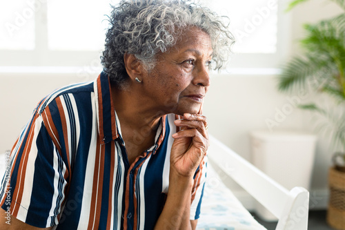 Portrait of thoughtful african american senior woman sitting on bed and look into distance