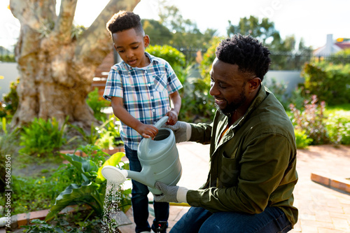Happy african american father and son watering plants together