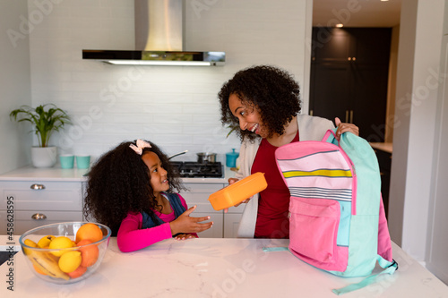 Happy african american mother and daughter preparing lunchbox for school photo