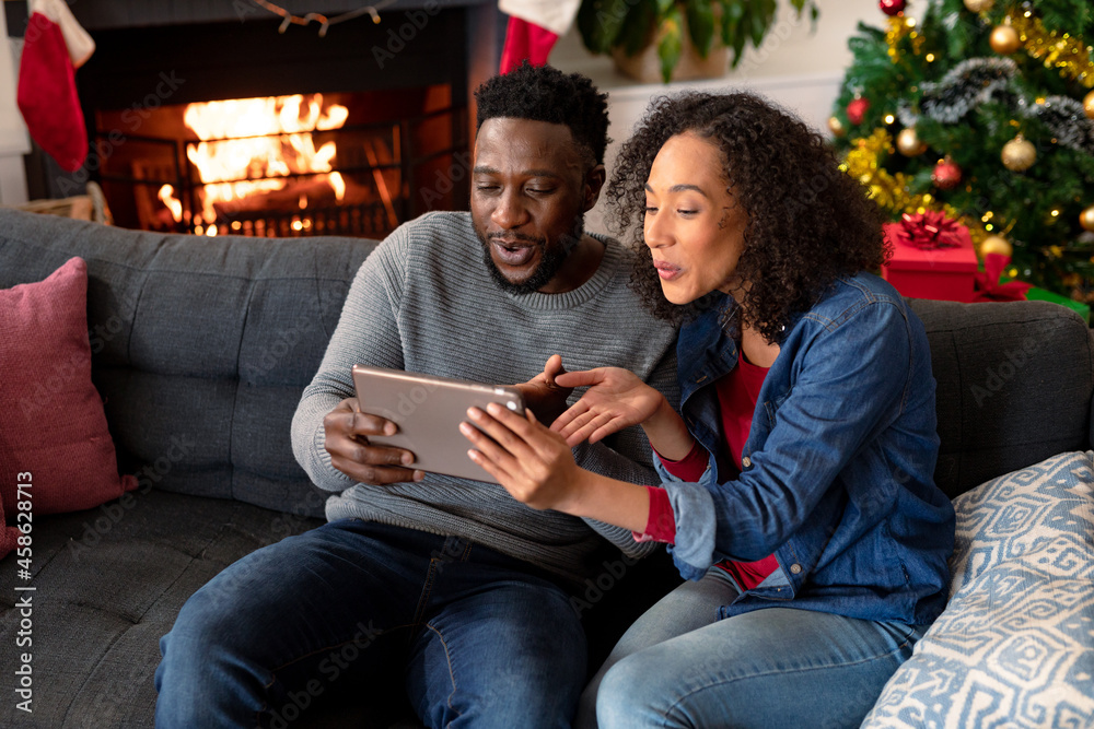 Happy african american couple having video call on tablet, christmas decorations in background