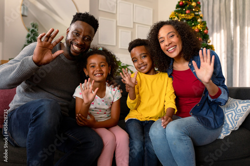 Happy african american family waving, having video call, christmas decorations in background