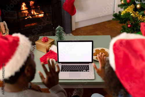 Back view of african american couple wearing santa hats, using laptop with copy space on screen